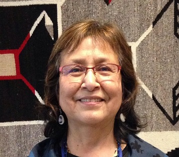 headshot of a woman with shoulder-length brown hair and glasses in front of a grey, black, and red weaving